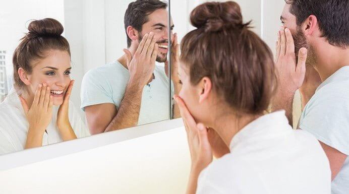 Happy man and woman with clear skin smiling in mirror after using MD Acne Kit from MD Skin Collection.